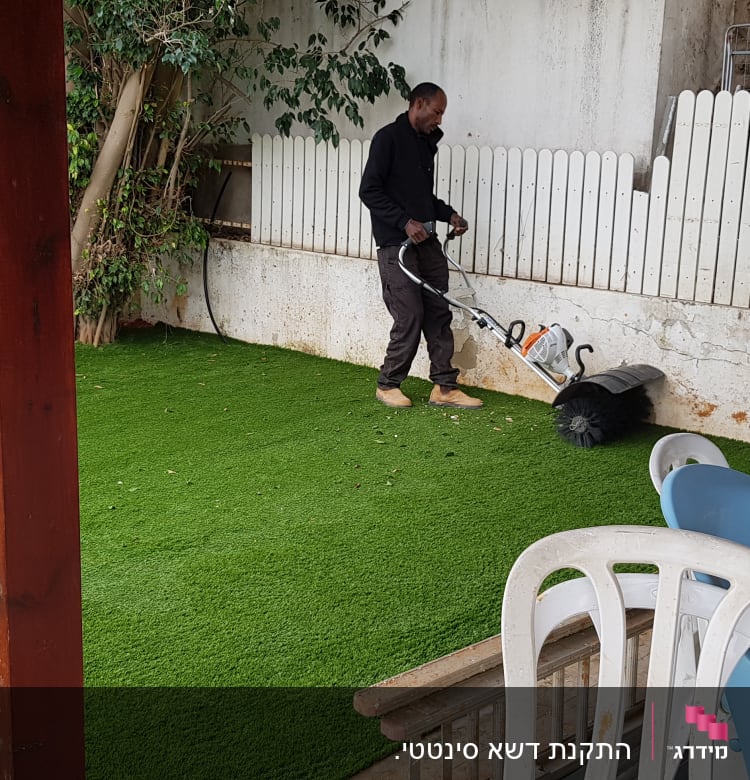 אדם משתמש במכונת ניקוי דשא סינתטי בגינה